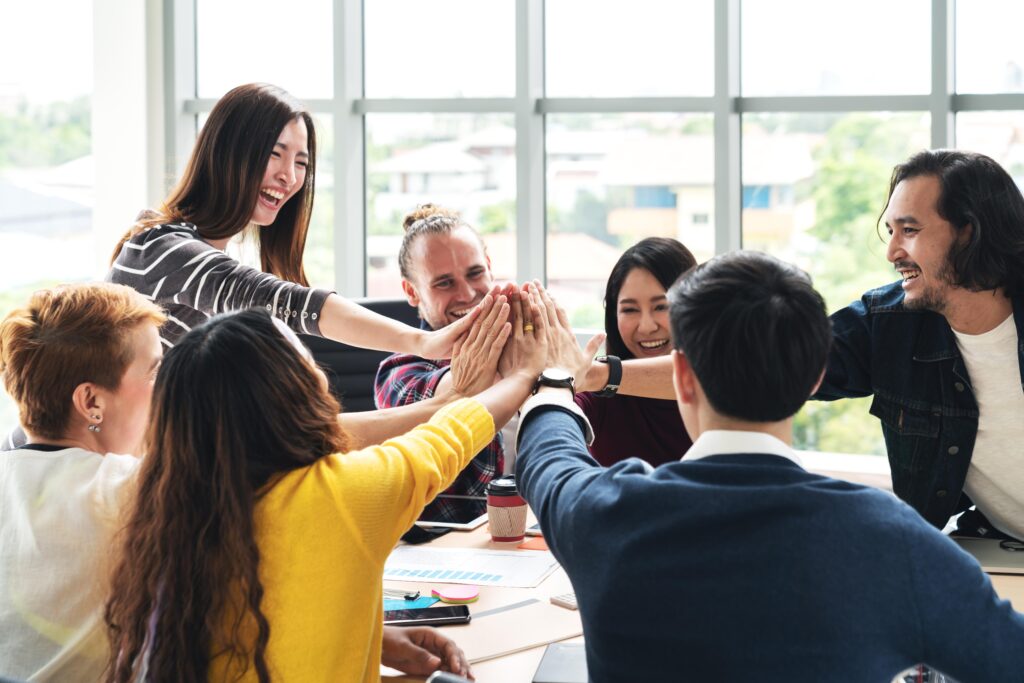 Colleagues celebrating success with a group high-five in a bright office.